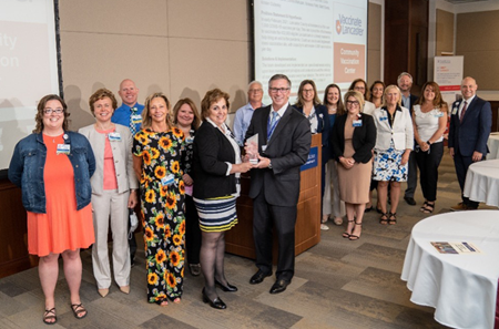 The large Community Vaccination Center team poses with their CEO Award, along with John J. Herman in a conference room